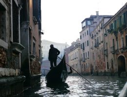 man in black jacket riding on boat on river between buildings during daytime