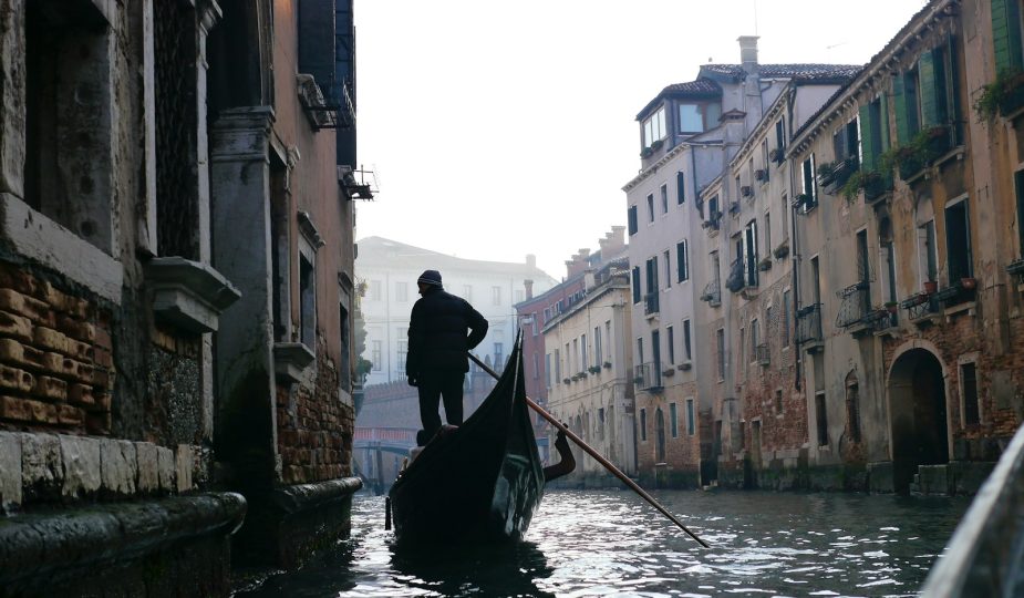 man in black jacket riding on boat on river between buildings during daytime